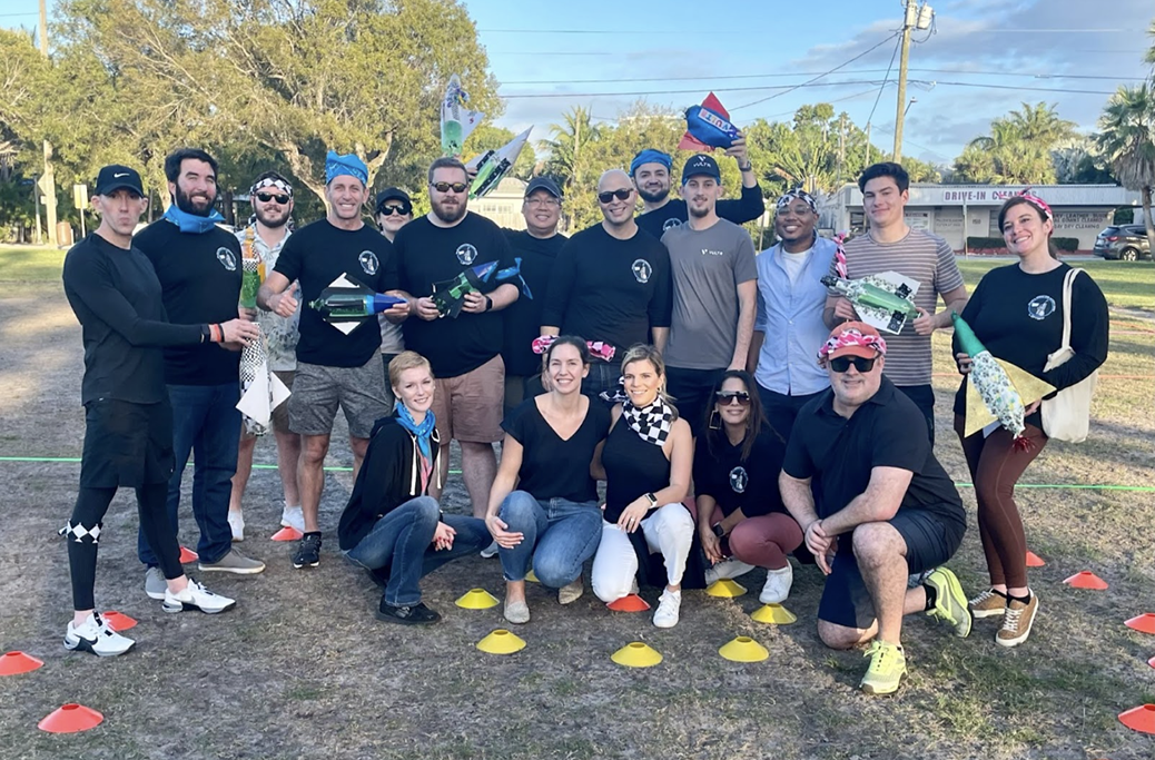 A group picture at the Sales and Marketing kickoff, smiling and showing off their homemade rockets.